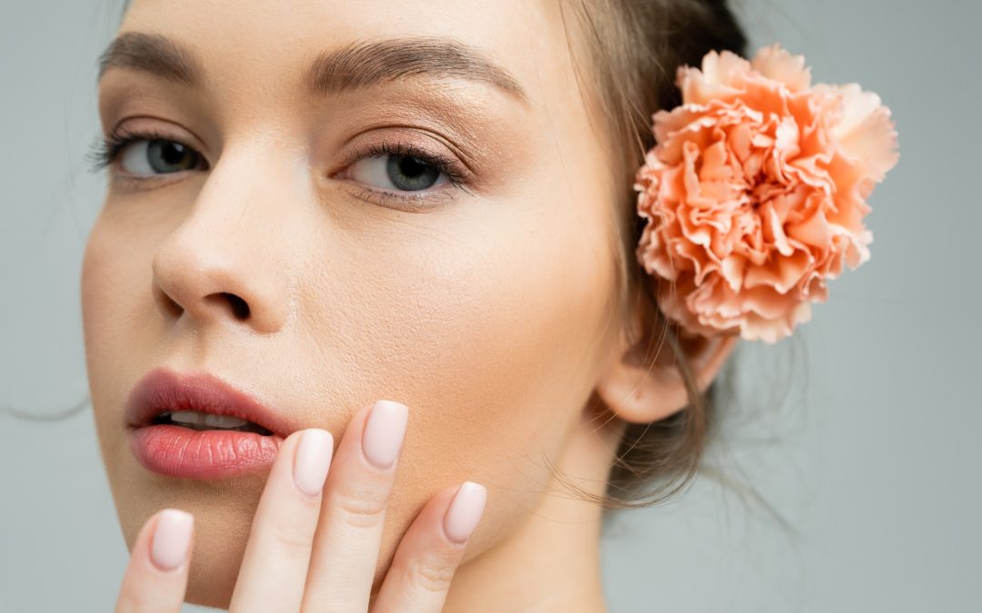 close up portrait of sensual woman with natural makeup and peach carnation behind ear touching face